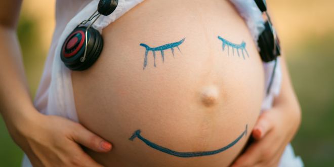 Schwangere Frau mit auf den Bauch gemaltem Smiley